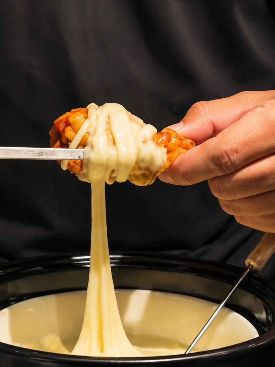 Alita envuelta en queso mozzarella derretido saliendo de la cacerola de fondue