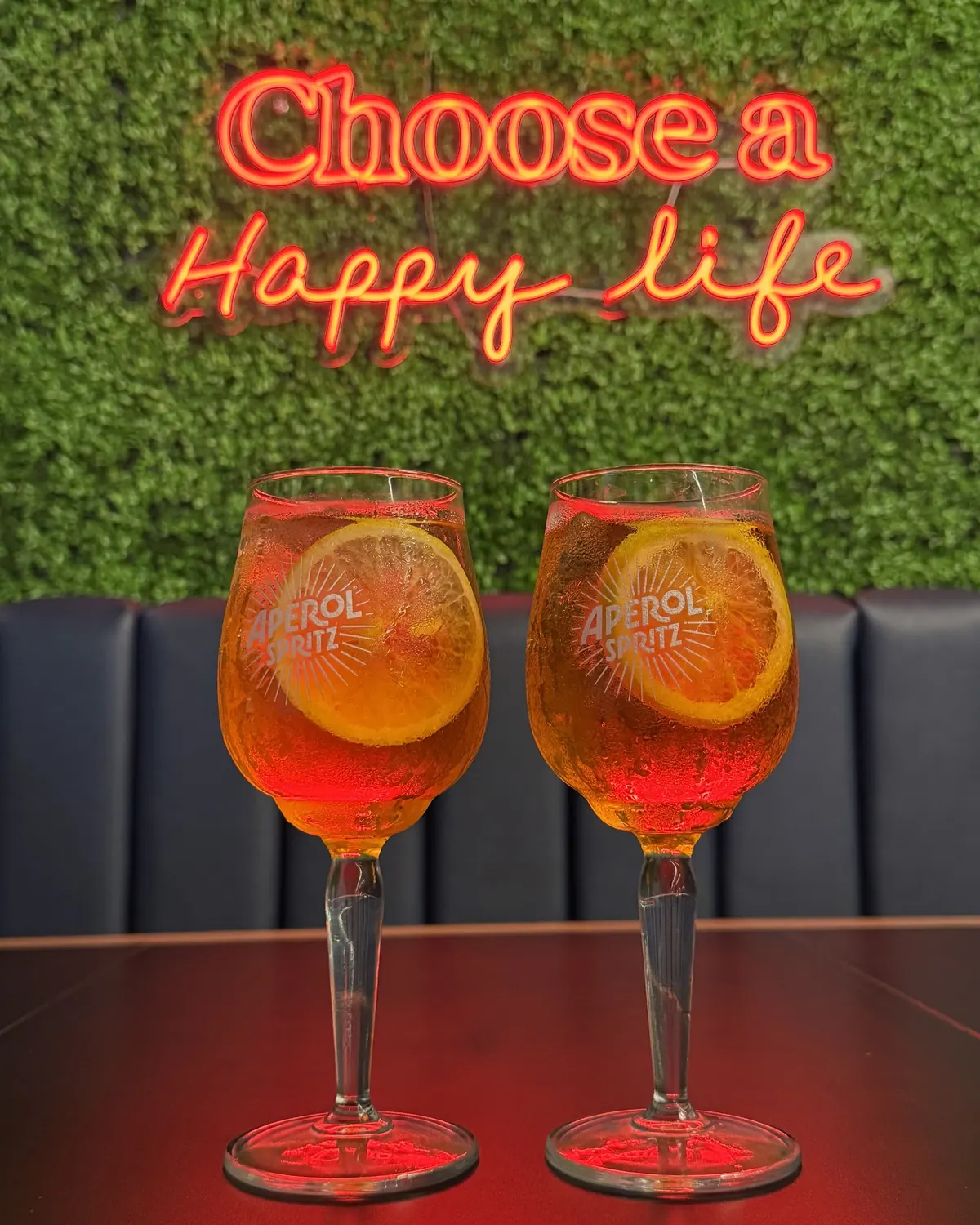 Copas de Aperol Spritz frente al letrero de neón Choose a Happy life