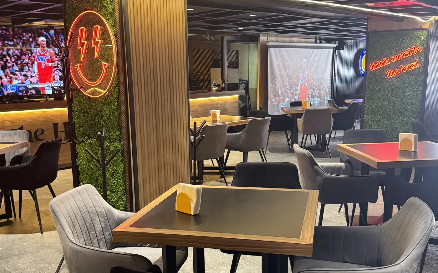 Salón con mesas y pantallas transmitiendo básquetbol